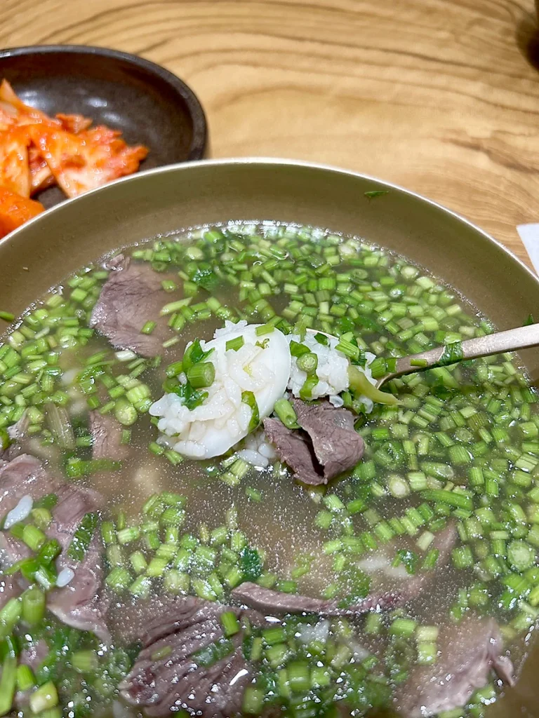 Kuah bening Geumnyeong Gomtang dengan minari hijau segar dan irisan daging